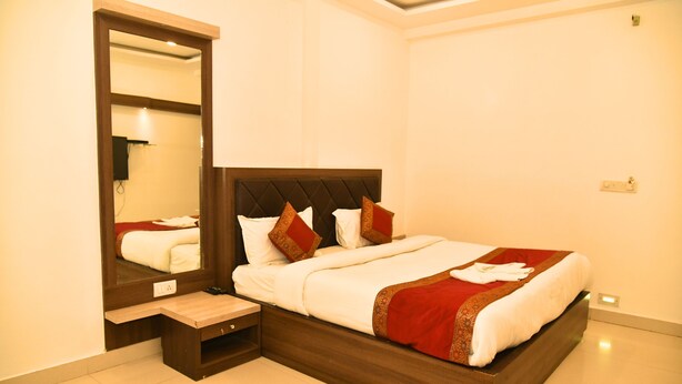 A neatly made bed with a wooden headboard, a bedside table, and a large mirror on the wall. - Hotel MM Continental (Varanasi)