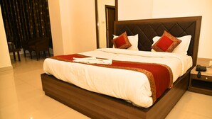 A neatly made bed with a dark headboard, white bedding, and red decorative pillows. - Hotel MM Continental (Varanasi)