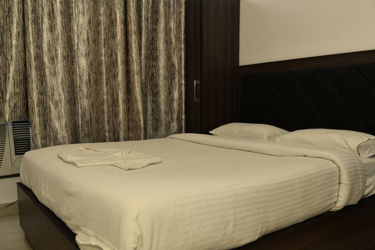 Una cama bien tendida con sábanas blancas en una habitación de hotel con cabecera oscura y pared de madera.