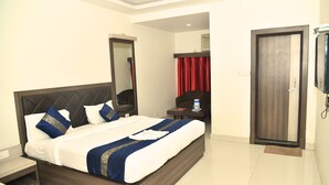 A hotel room with a large bed, a bedside table, a mirror, a wardrobe, and a television. - Hotel MM Continental (Varanasi)