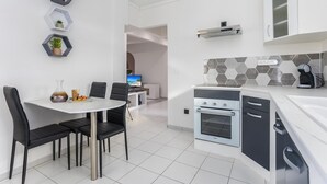A modern kitchen with a white countertop, black cabinets, and a hexagonal backsplash. There is a dining area with a white table and black chairs.