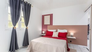 A bedroom with a bed, curtains, a nightstand, a wall-mounted light, and a framed picture.