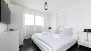 A modern hotel room with a large bed, white walls, a flat-screen TV, and a ceiling-mounted light fixture. - Cozy home in Olpenitz with sauna (Olpenitz)