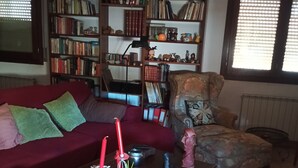 A living room with a red sofa, a patterned armchair, a coffee table with decorative items, and a bookshelf filled with books and knick-knacks. - LOFT CASTELLÓ 110m2 apartment. Pets welcome! (Castelló de Farfanya)