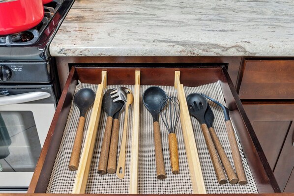 A kitchen drawer with wooden utensils and a red pot on the stove.