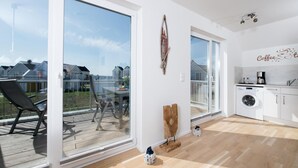 A modern apartment with a balcony, a dining area, a kitchen, and a large window offering a view of other buildings. - Nice apartment in Olpenitz with sauna (Olpenitz)