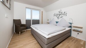 A modern bedroom with a bed, a chair, a desk, and a large window. - Nice apartment in Olpenitz with sauna (Olpenitz)
