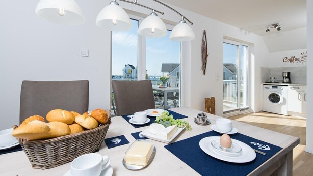 A modern kitchen with a view of the city, a dining area with a table set for breakfast, and a washing machine in the background. - Nice apartment in Olpenitz with sauna (Olpenitz)