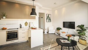 Une cuisine moderne dotée d’un îlot central, un coin repas avec une table noire et un espace de vie comprenant un téléviseur et des plantes.