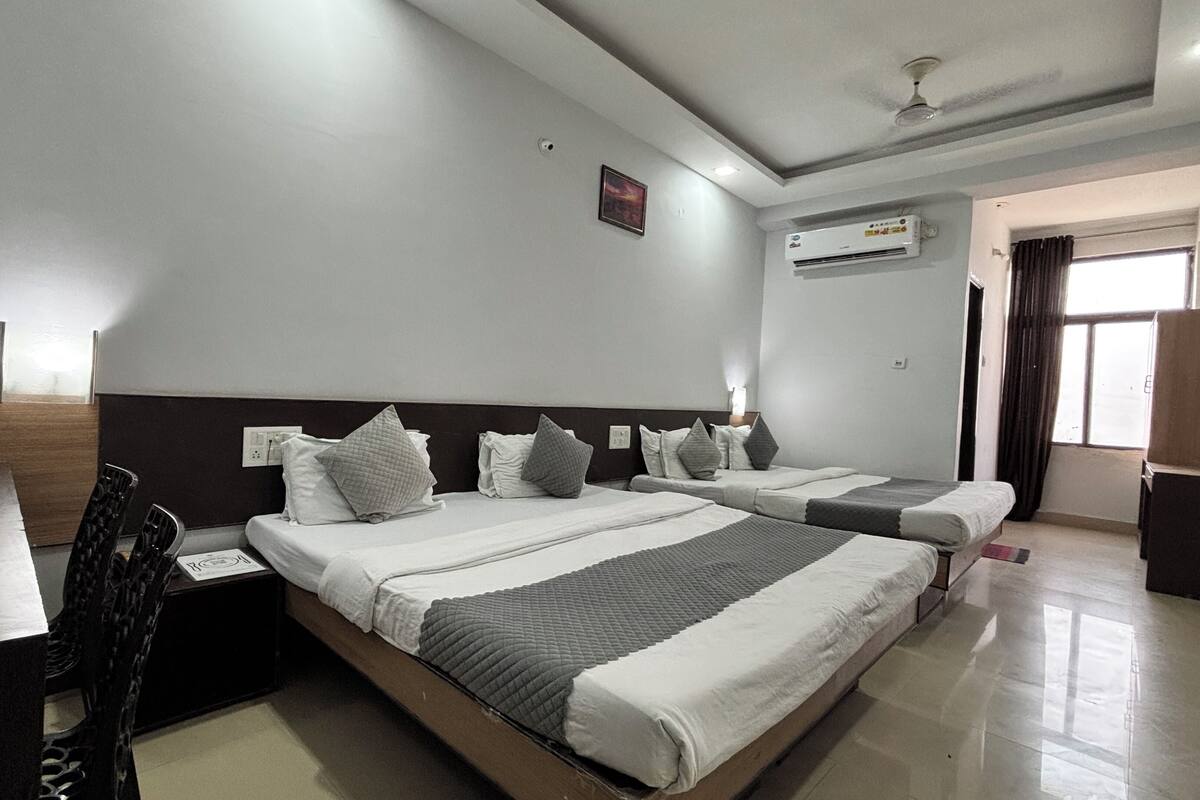 A hotel room with two beds, a desk, a chair, an air conditioning unit, and a window with curtains.