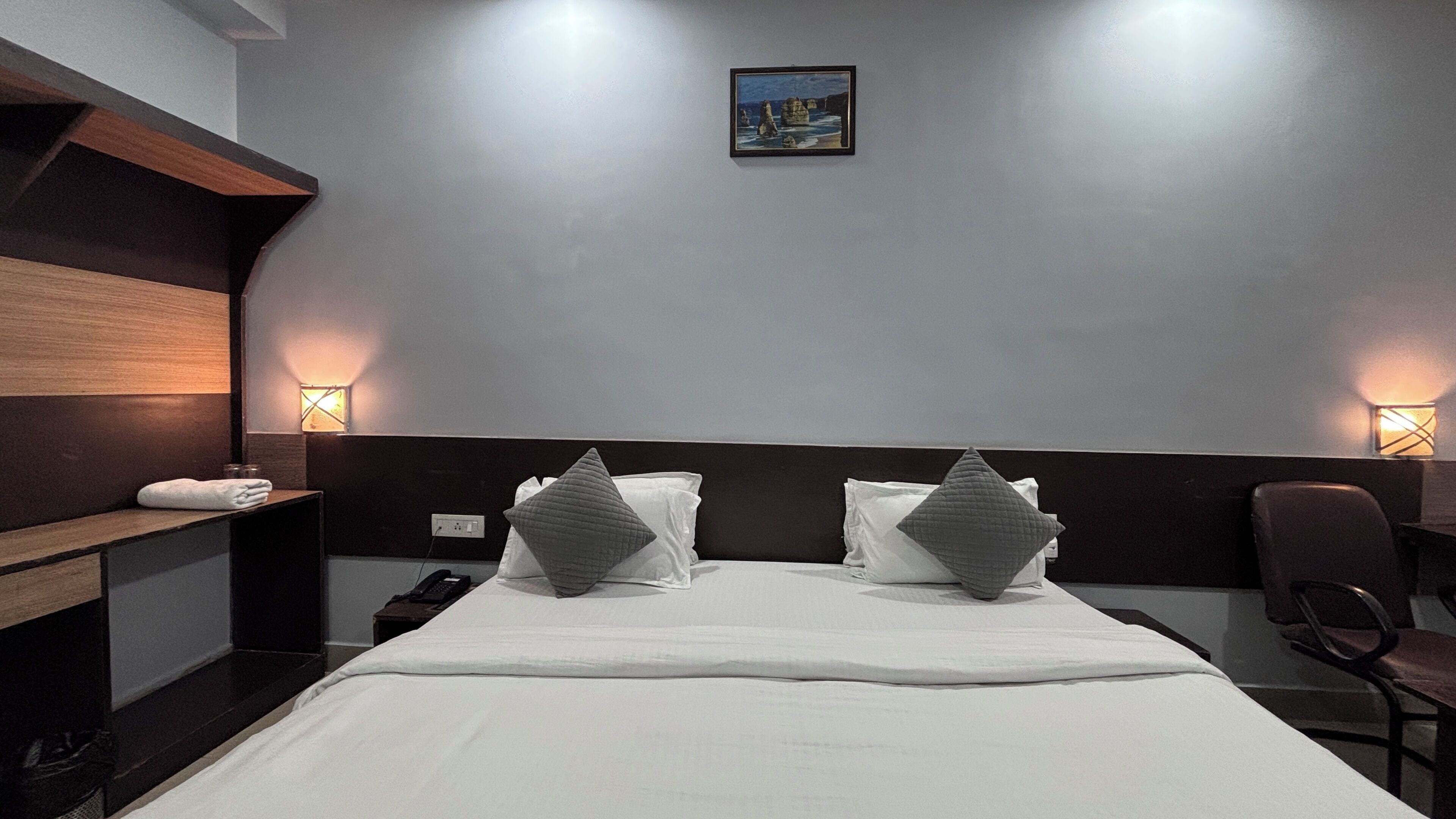 Ein Hotelzimmer mit einem Bett, Nachttischlampen, einem Nachttisch, einem Sessel und einem Bild an der Wand.