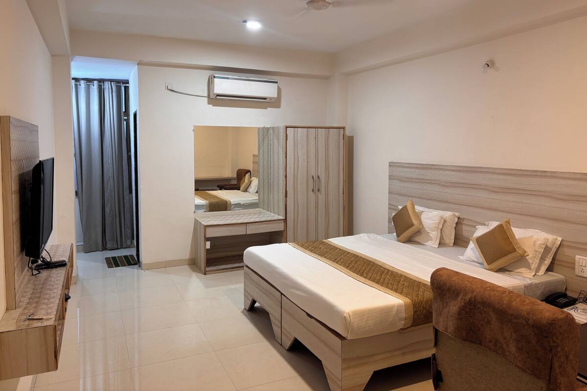 A hotel room with a bed, a desk with a TV, a wardrobe, and a ceiling fan.