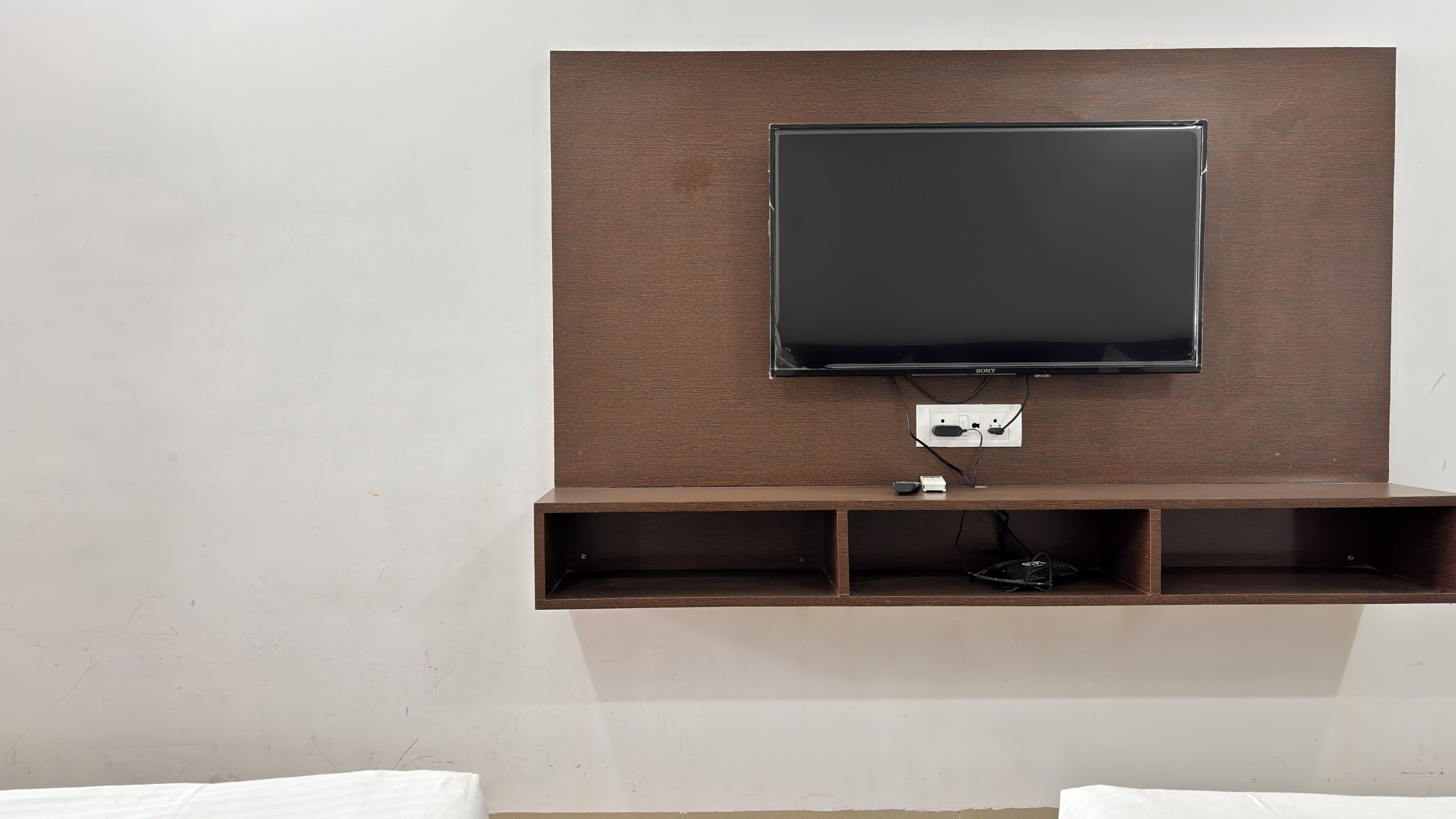 A wall-mounted TV with a wooden panel, a power outlet, and a shelf below.