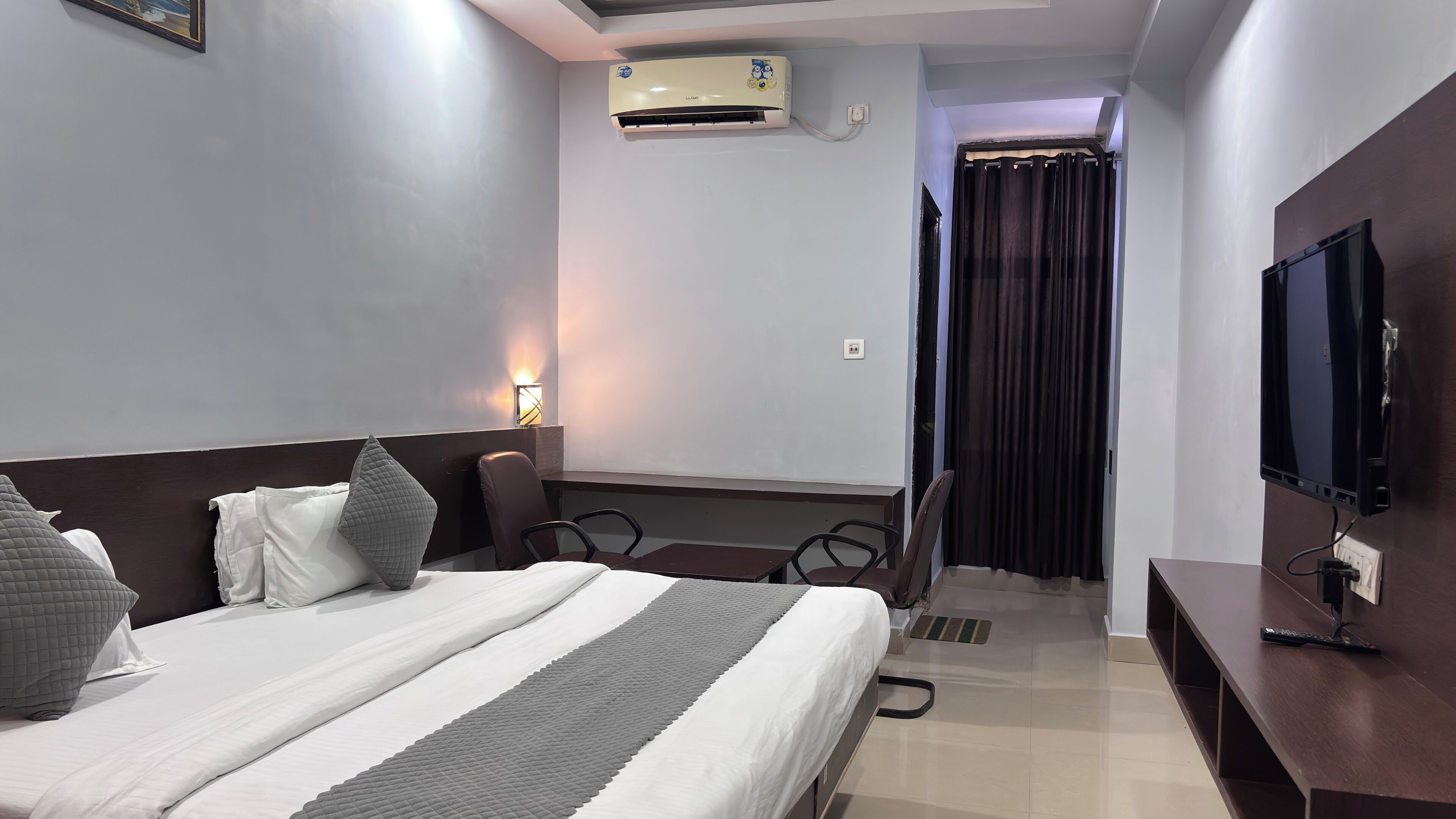 Ein Hotelzimmer mit Bett, Schreibtisch, Fernseher, Klimaanlage und Vorhang.