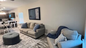 Un salon avec un canapé gris, un pouf et un tapis à motifs.