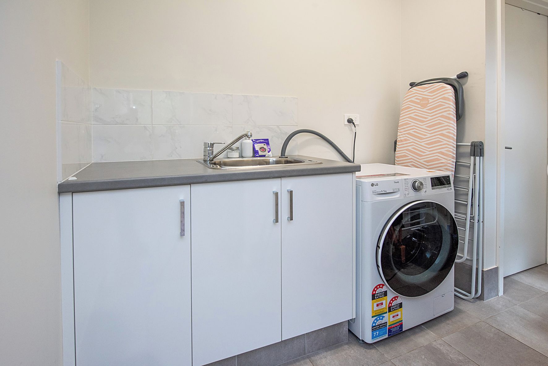 A laundry room with a washing machine, a drying rack, and a sink with a marble backsplash.