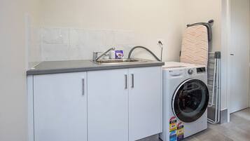 A laundry room with a washing machine, a drying rack, and a sink with a marble backsplash.