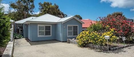 A residential property with a single-story structure, a front porch, and a small garden with flowering plants.