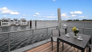 A deck with a table and chairs, overlooking a body of water with boats and a dock in the background. - Beach front ship in Olpenitz with sauna (Olpenitz)