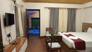 A hotel room with a wooden ceiling, a TV mounted on the wall, a bed with a red blanket, a desk with a laptop, and a small table with a chair. - GHARANA RESORT (Chandannagar)