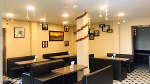 A restaurant with booths and tables, decorated with hanging lights and framed pictures on the walls. - GHARANA RESORT (Chandannagar)