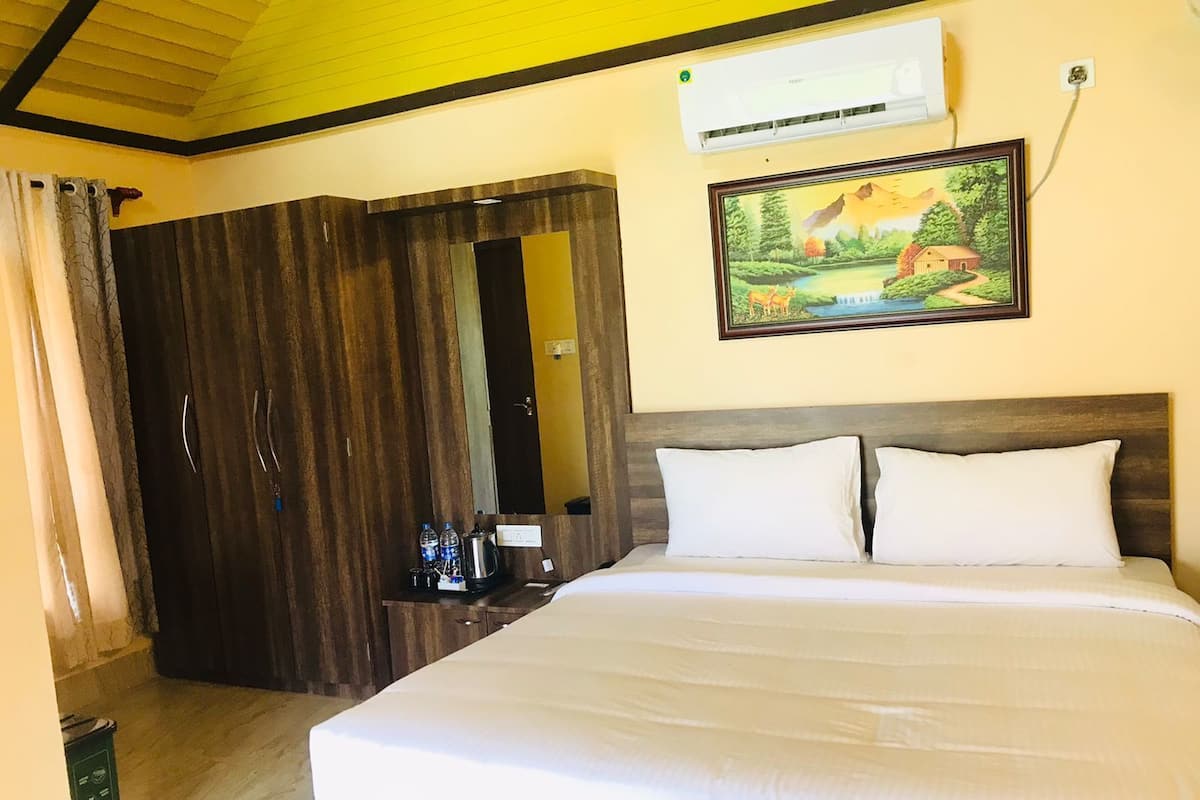 A hotel room with a large bed, a wardrobe, an air conditioning unit, and a painting on the wall.