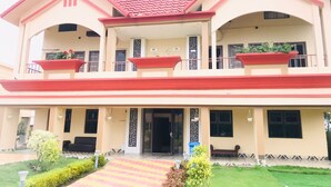 A two-story building with a red-tiled roof, balconies with flower planters, and a front entrance with a set of stairs leading up to it. - GHARANA RESORT (Chandannagar)