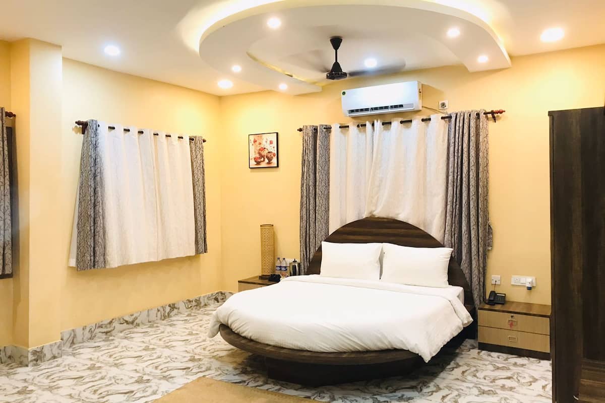A bedroom with a round bed, a ceiling fan, an air conditioning unit, and a patterned carpet.