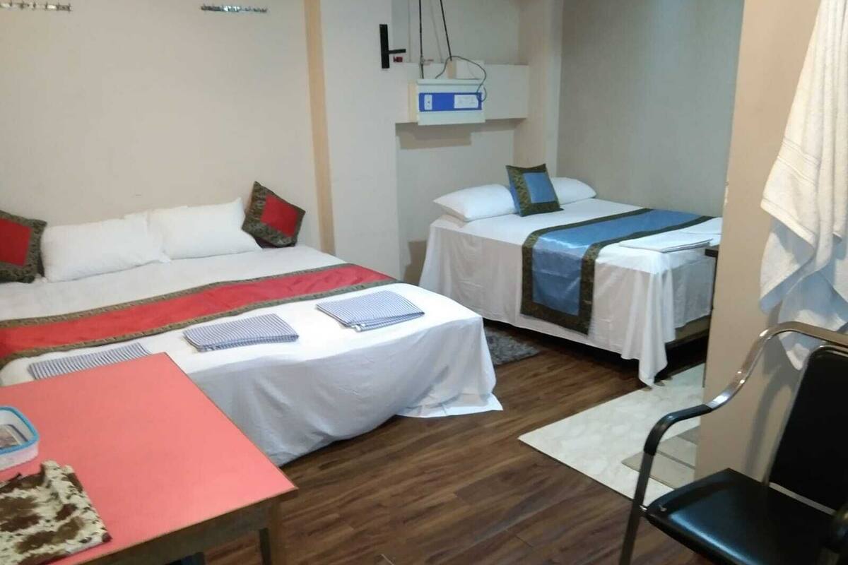 Habitación de hotel con dos camas, un escritorio, una silla y una mesita con mantel rojo.
