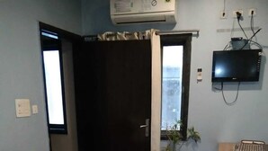 A hotel room with a bed, a TV, a window, and a plant. - Hotel Medwin Kashi Dham (Varanasi)