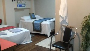 A hotel room with two beds, a desk, a chair, a ceiling fan, and a potted plant. - Hotel Medwin Kashi Dham (Varanasi)