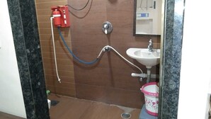 A bathroom with a shower, sink, and a red fire extinguisher mounted on the wall. - Hotel Medwin Kashi Dham (Varanasi)