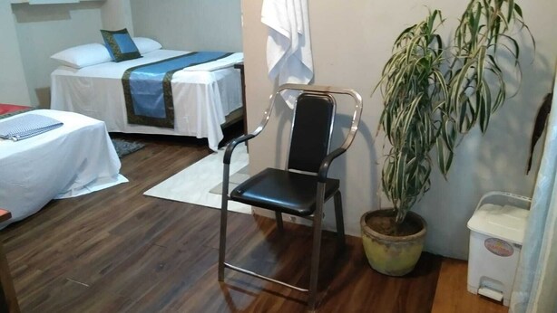 A hotel room with a bed, a chair, a small table, a potted plant, and a trash bin. - Hotel Medwin Kashi Dham (Varanasi)