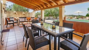 An outdoor patio with wicker furniture, a glass-top table, and a view of a pool and greenery. - Finca in Mallorca with Private Pool & Views (Son Macià)