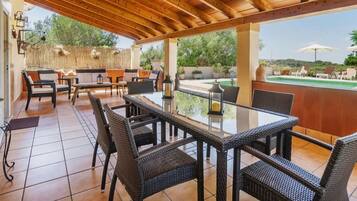 An outdoor patio with wicker furniture, a glass-top table, and a view of a pool and greenery.