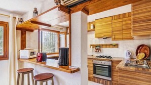 A compact kitchen with wooden cabinets, a microwave, a stove, and a sink. There are two stools and a window providing natural light. - Finca in Mallorca with Private Pool & Views (Son Macià)