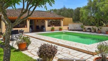 A house with a tiled roof, a swimming pool, and potted plants.