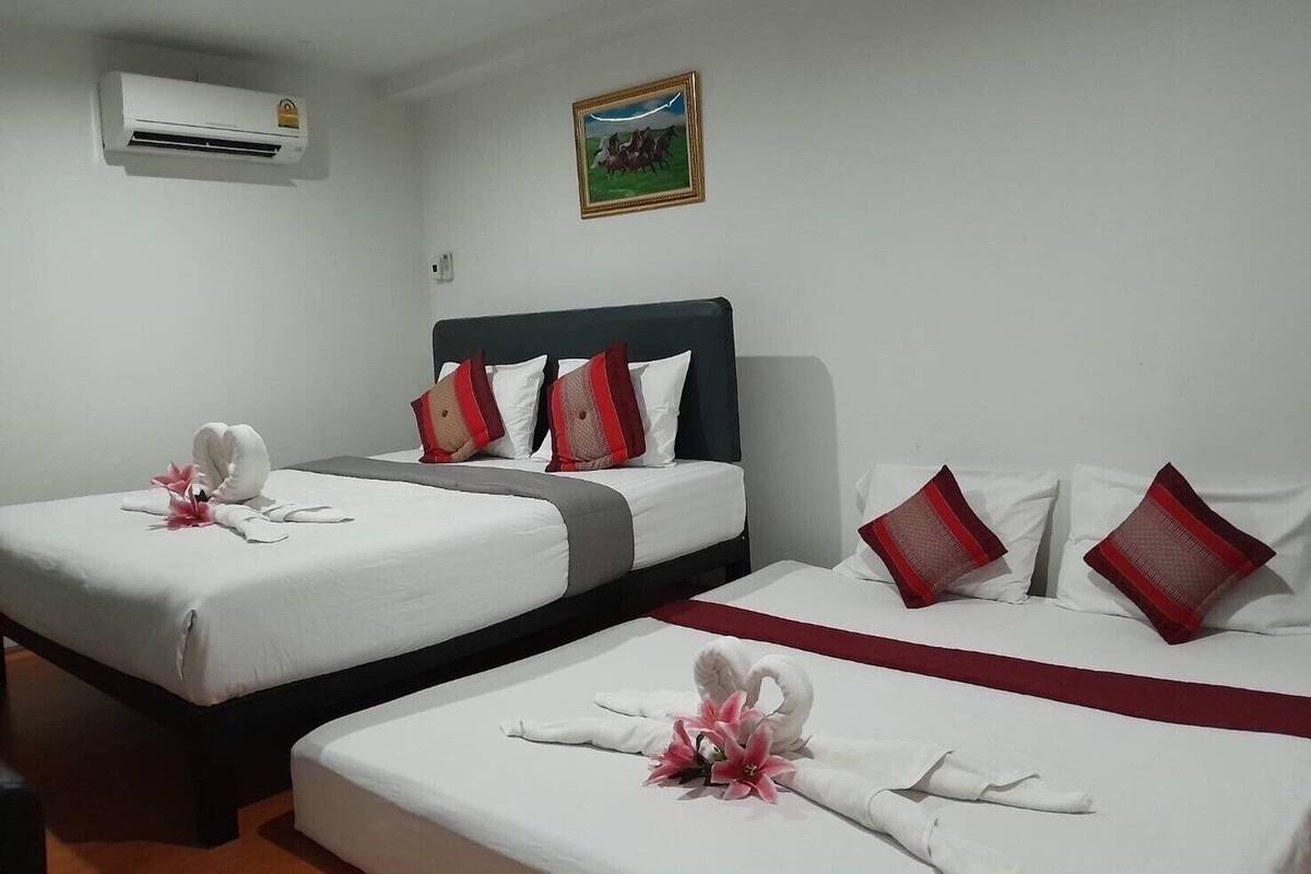 A hotel room with two beds, each with white linens, red pillows, and decorative swans made from towels. An air conditioning unit is mounted on the wall, and a framed picture hangs above the beds.
