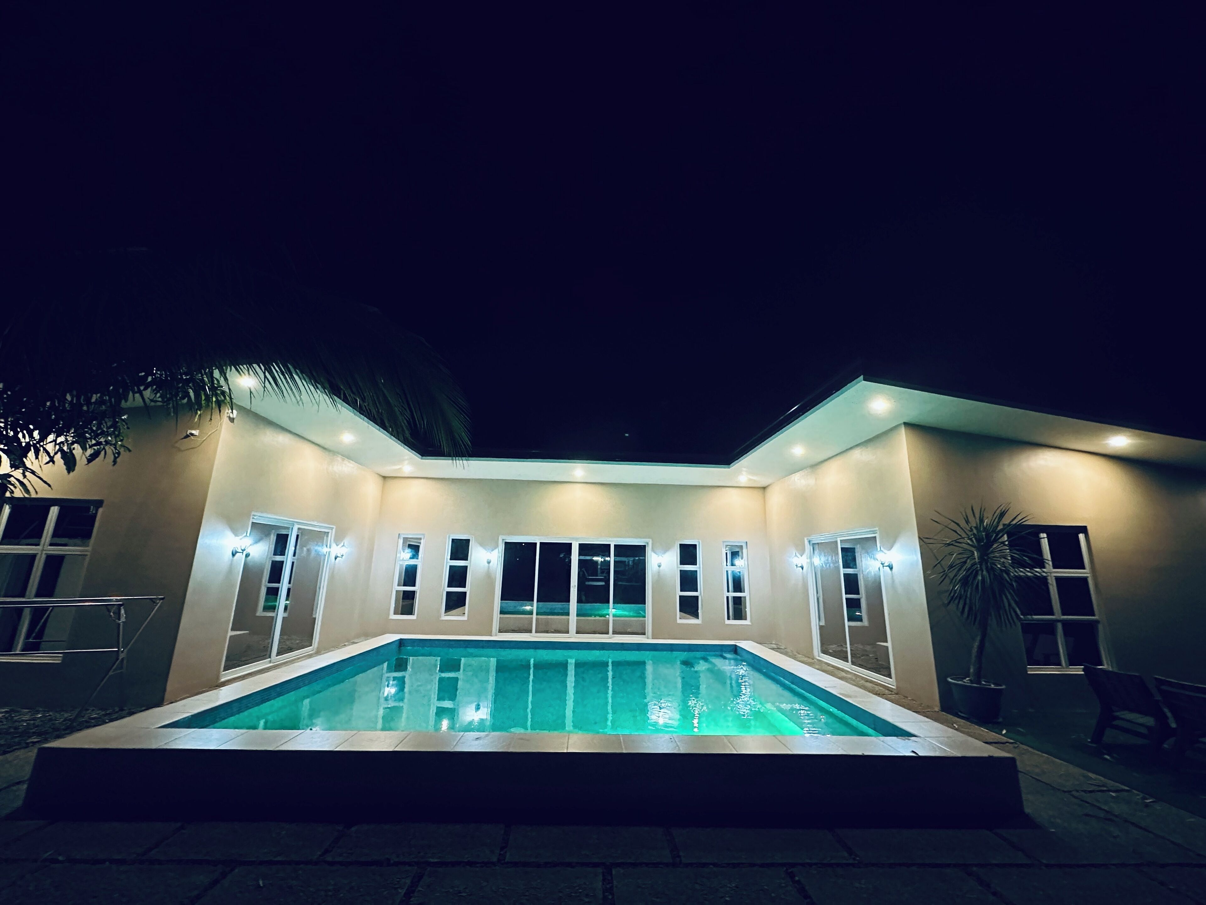 A modern house with a swimming pool, multiple windows, and a well-lit exterior at night.