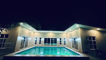 A modern house with a swimming pool, multiple windows, and a well-lit exterior at night.