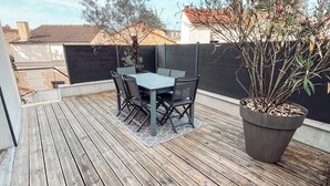A wooden deck with a table and chairs, surrounded by a black fence and potted plants. - NEW Duplex Hyper Centre Avec Piscine (Bergerac)