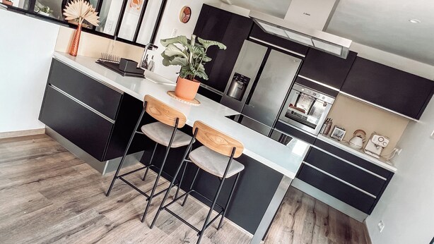 A modern kitchen with a central island, bar stools, a potted plant, and built-in appliances. - NEW Duplex Hyper Centre Avec Piscine (Bergerac)