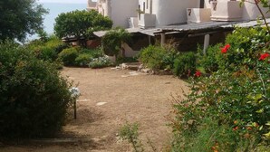 A courtyard with a gravel path, surrounded by lush greenery and a building with a white facade. - Villa a few steps from the sea of Villasimius (Villasimius)