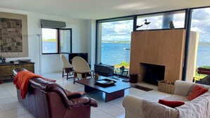 Una sala de estar moderna con chimenea, ventanas amplias con vistas a un cuerpo de agua y asientos cómodos.