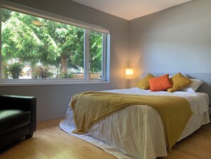 A bedroom with a large window, a bed with white bedding and a yellow throw, and a black chair. - 3 BR Seaside Bliss-Close to the beach-OCEAN VIEW! (White Rock)