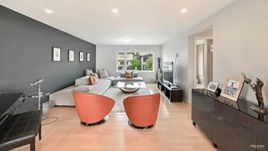 A modern living room with a grey sofa, orange chairs, a piano, and a TV.