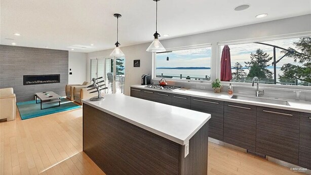 A modern kitchen with a large island, dark wood cabinets, and a view of the sea.
