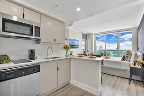 A modern kitchen with a built-in microwave, a coffee machine, and a dishwasher. There is a dining area with a table set for two and a view of the cityscape through large windows. - Spectacular View Suite - Coconut Grove Oasis (Miami)