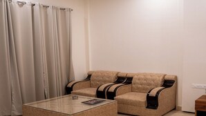 Una sala de estar con una mesa de centro de vidrio, dos sofás con detalles en negro y una cortina.