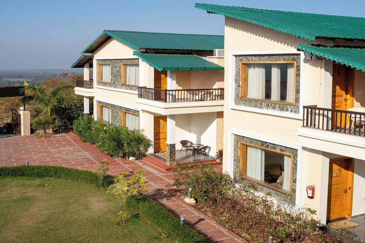 A two-story hotel with a green roof, a balcony with a wooden railing, and a stone pathway leading to the entrance.